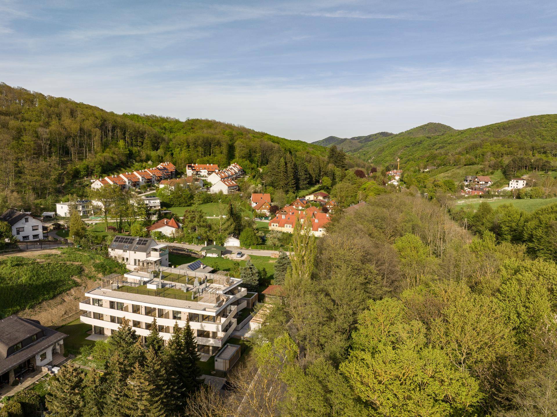 Panoramablick auf das Apartmentgebäude und die umliegende Wohnsiedlung in einer grünen Berglandschaft.