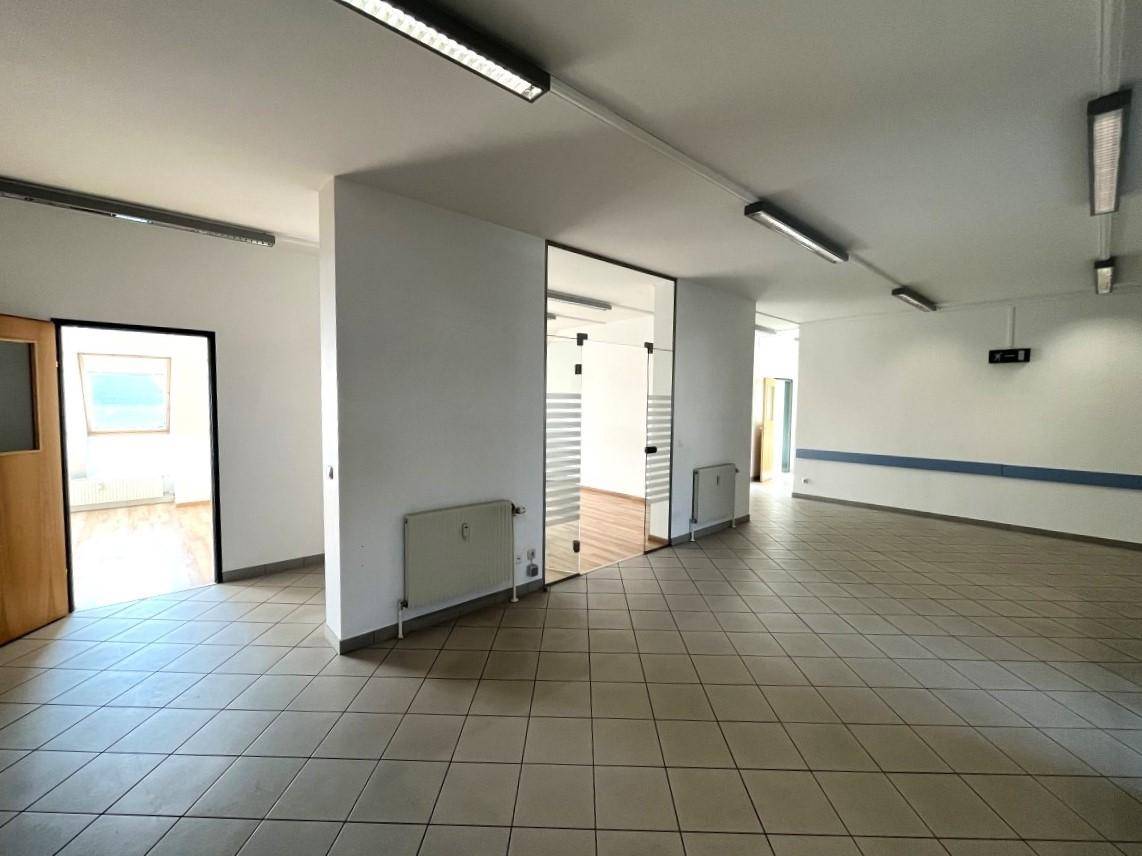 Geräumiger, heller Büroraum mit Fliesenboden, Glastüren und Blick in weitere Räume.