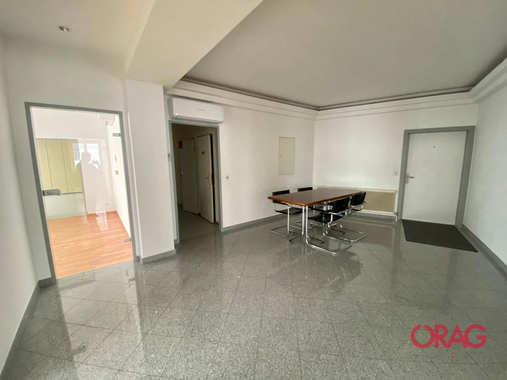 Geräumiger Bürobereich mit Fliesenboden, Heizkörpern und einem Konferenztisch.