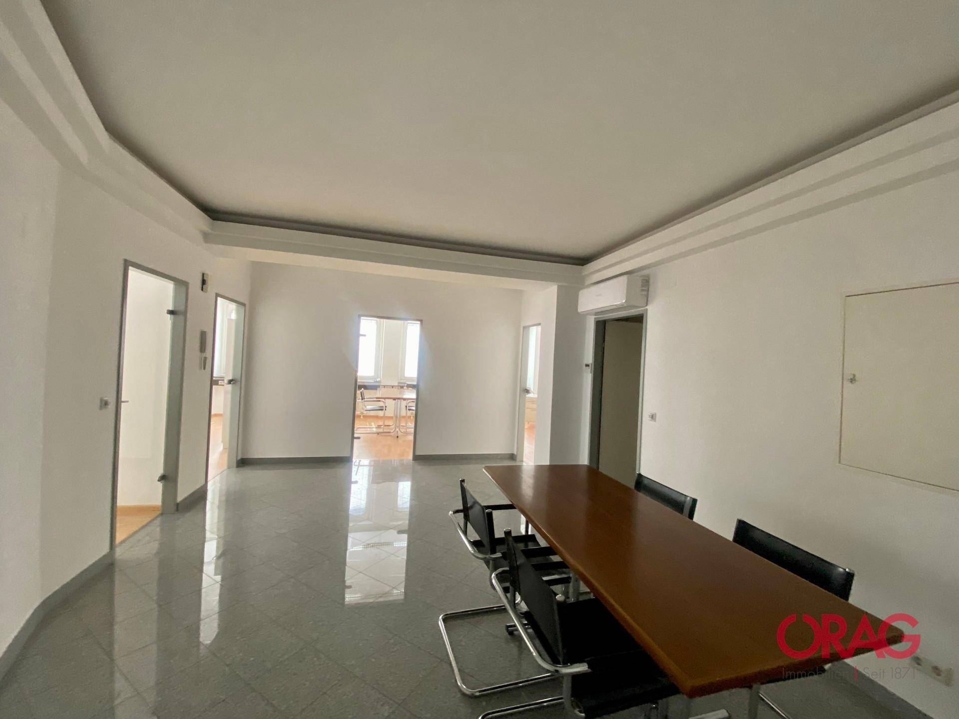 Heller Büroraum mit glänzendem Fliesenboden und einem langen Konferenztisch.