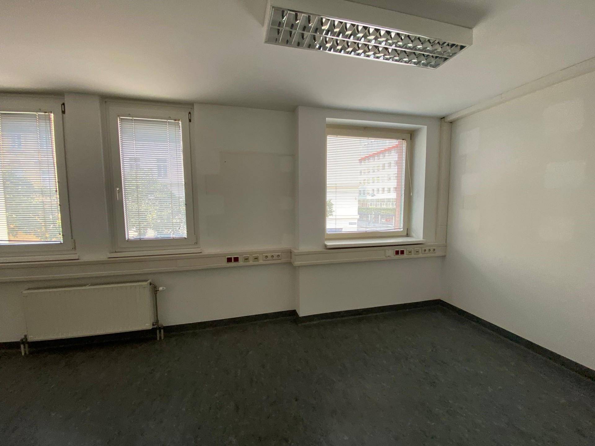 Leerer Büroraum mit einer Wand voller Fenster, die für viel Helligkeit sorgen und einen Blick nach draußen ermöglichen.