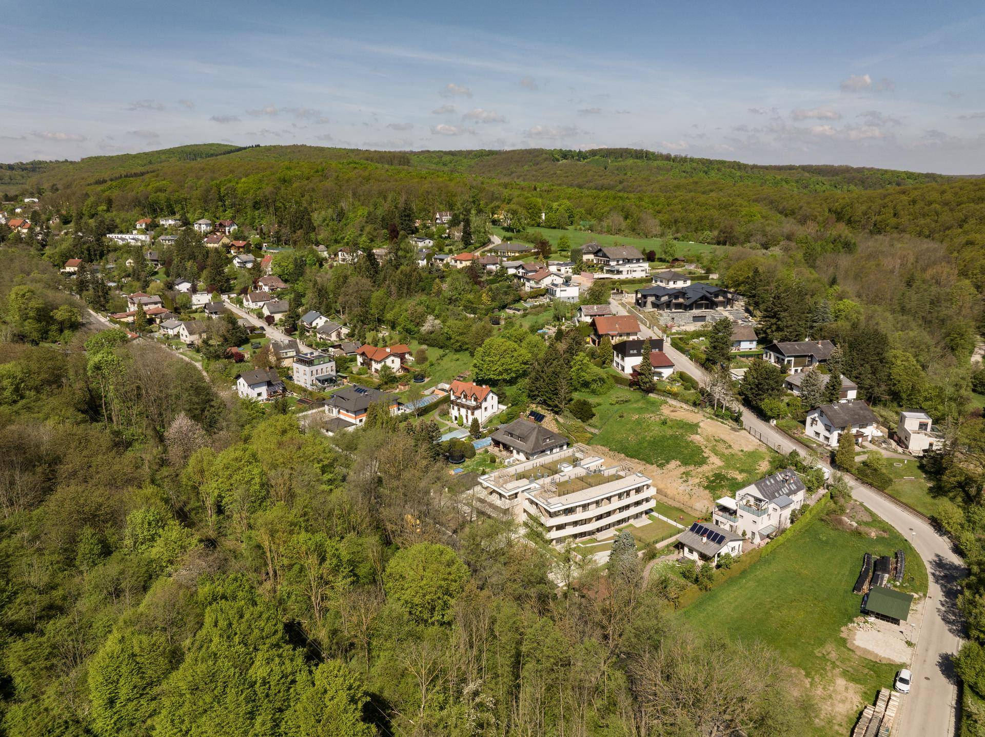 Weitläufige Luftaufnahme der Wohnsiedlung, eingebettet in eine grüne, hügelige Landschaft.