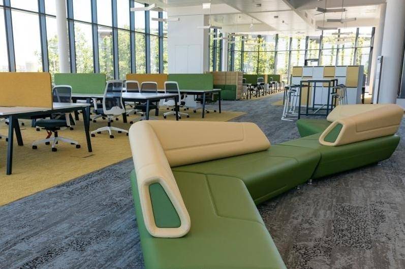 Moderner Großraumbüro-Bereich mit modularem Sofa, ergonomischen Arbeitsplätzen und viel Tageslicht.