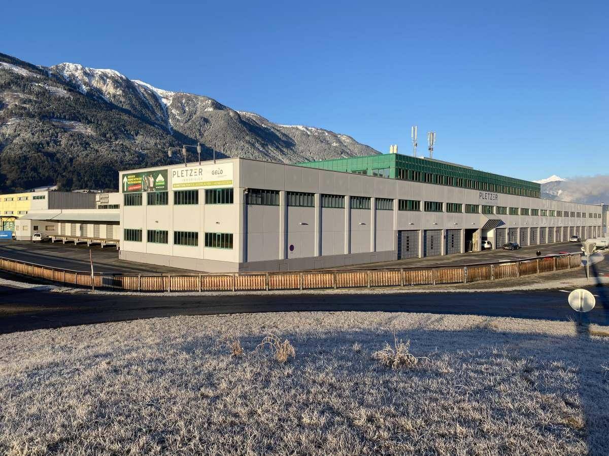 Großes Gewerbegebäude mit moderner Fassade vor einer beeindruckenden Bergkulisse im Winter.