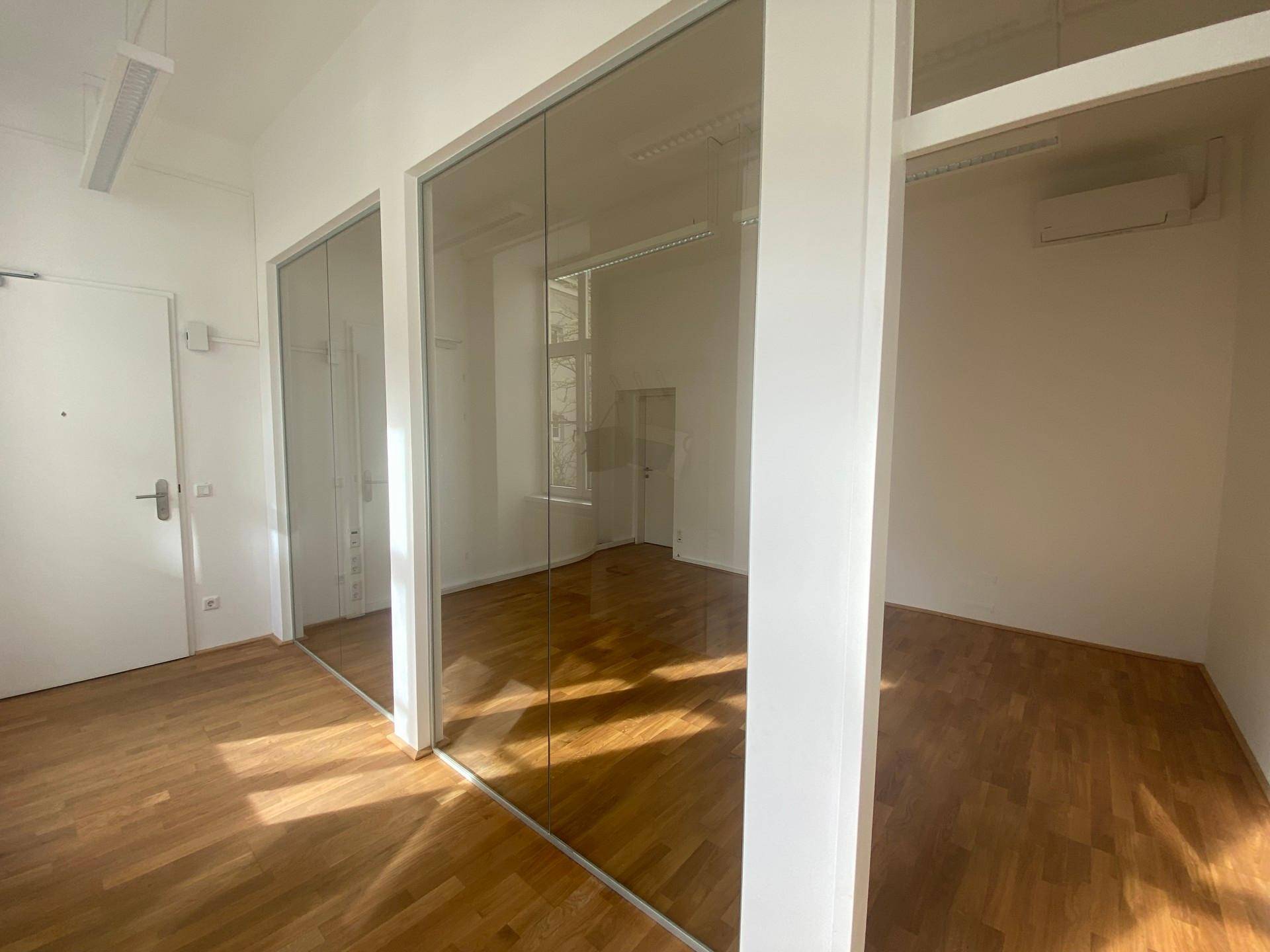 Heller Büroraum mit Holzboden und modernen Glaswänden, die den Raum unterteilen.