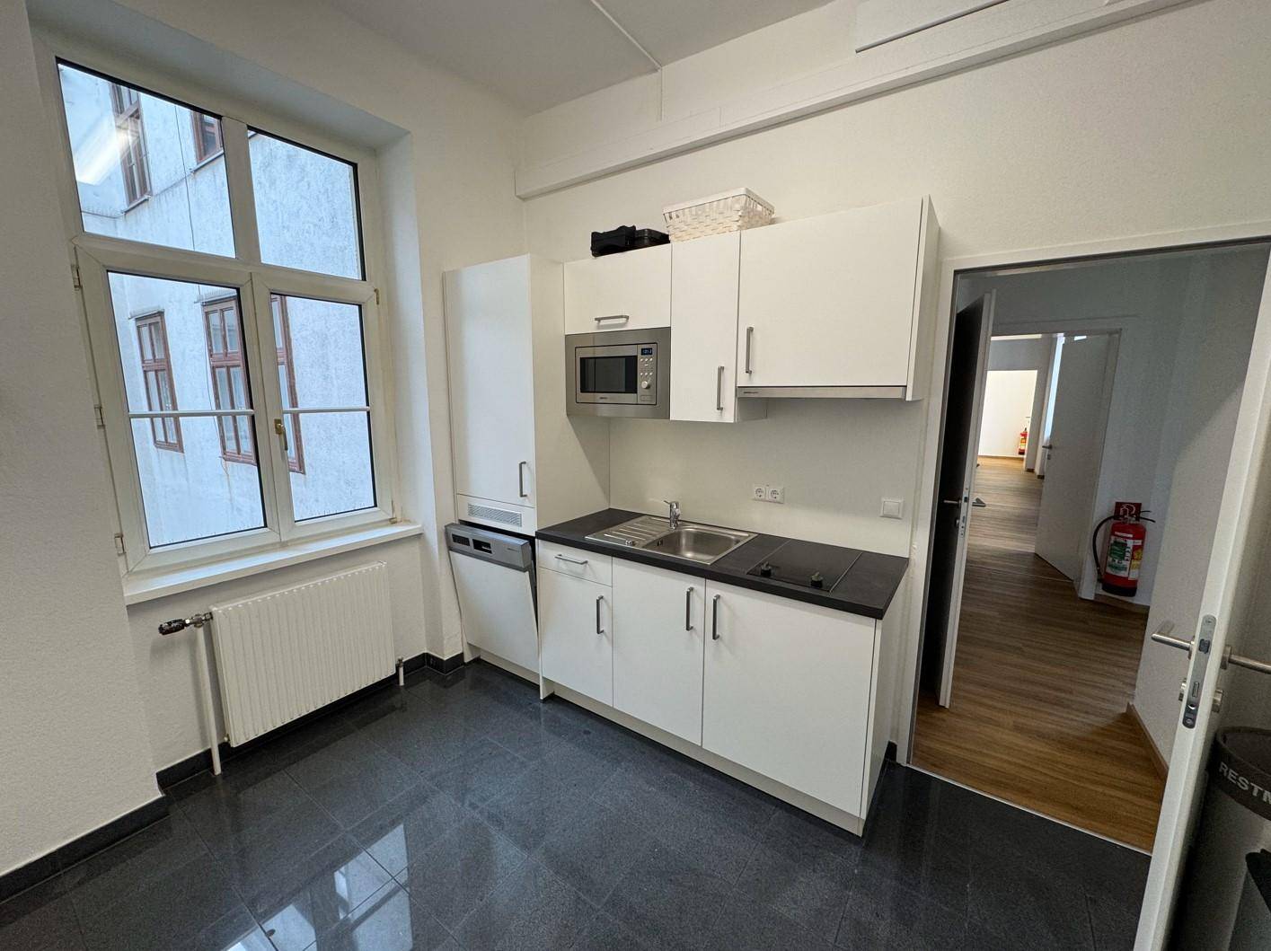 Kleine, funktionale Küchenzeile mit weißen Schränken, Spüle, Mikrowelle und Geschirrspüler.