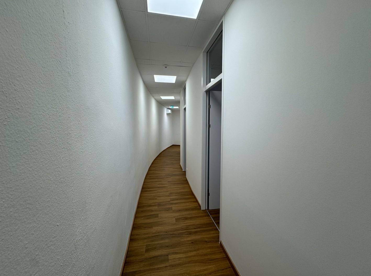 Langer, heller Flur mit Holzboden und Deckenleuchten, der zu weiteren Räumen führt.