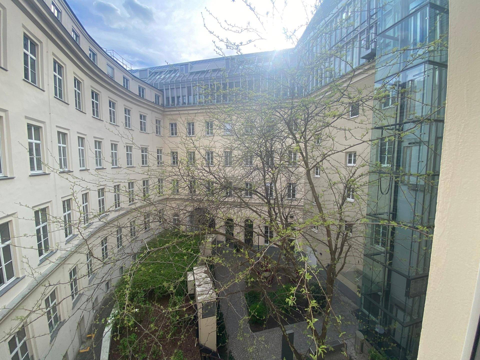 Blick von oben auf einen begrünten Innenhof mit Bäumen und moderner Glasfassade eines angrenzenden Gebäudes.