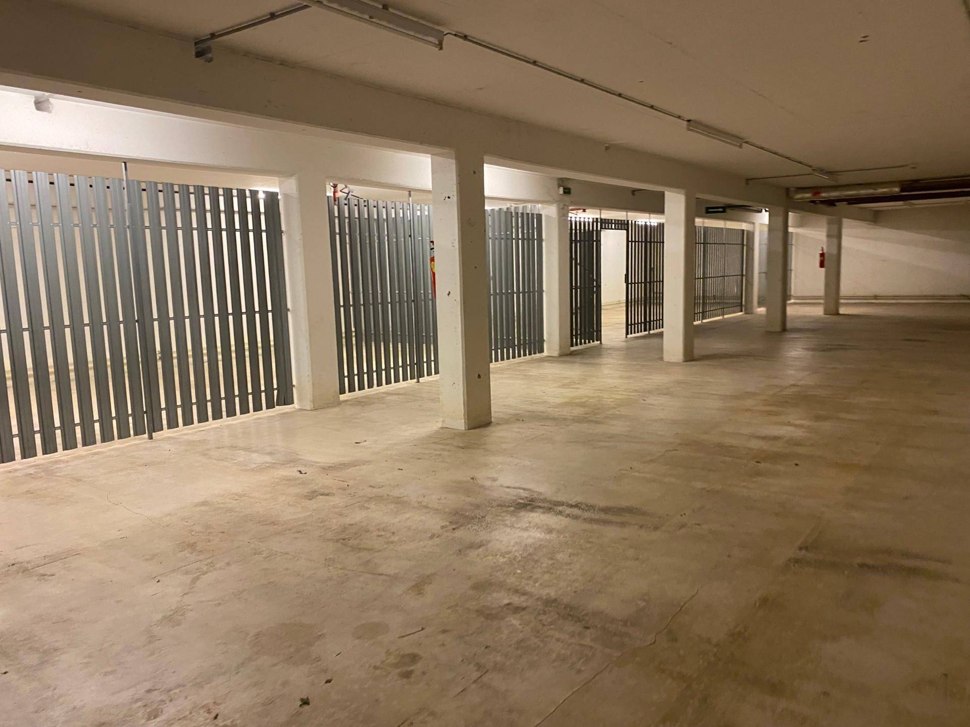 Leere Tiefgarage mit Betonboden, Säulen und Metallabtrennungen, die Parkplätze andeuten.