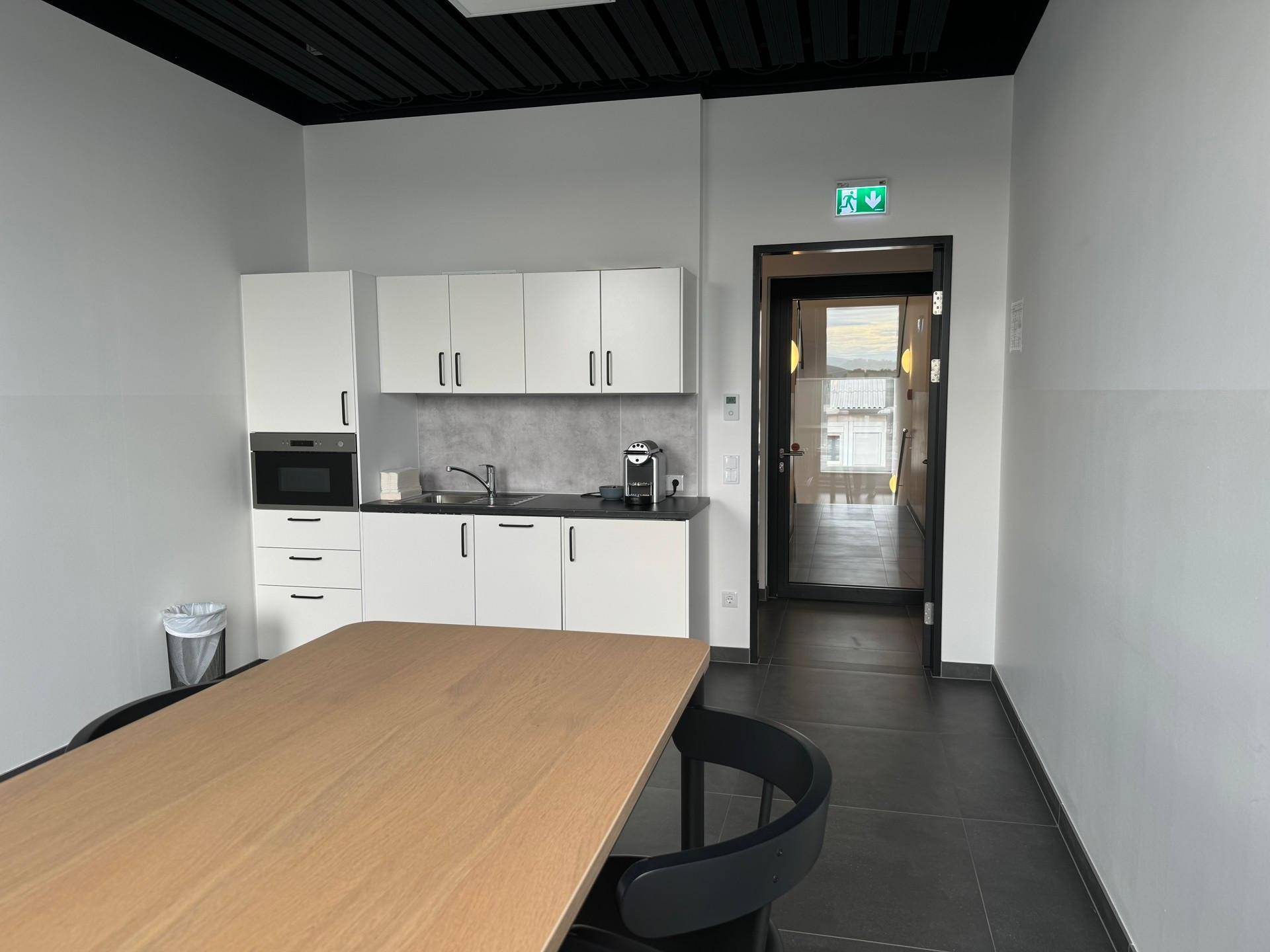 Kleine, moderne Teeküche mit weißen Schränken, integrierter Mikrowelle und Kaffeemaschine, ideal für Büropausen.