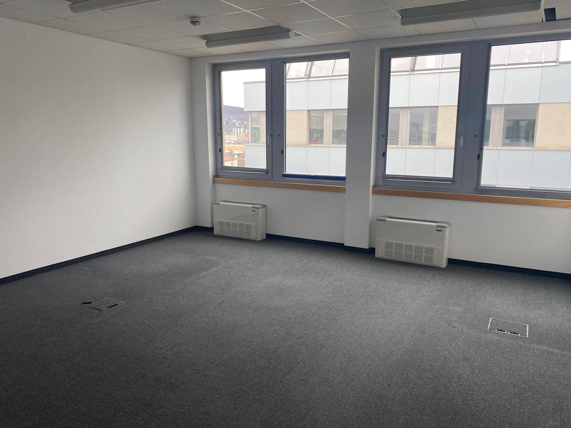 Helle Büroecke mit zwei großen Fenstern, Heizkörpern und grauem Teppichboden.