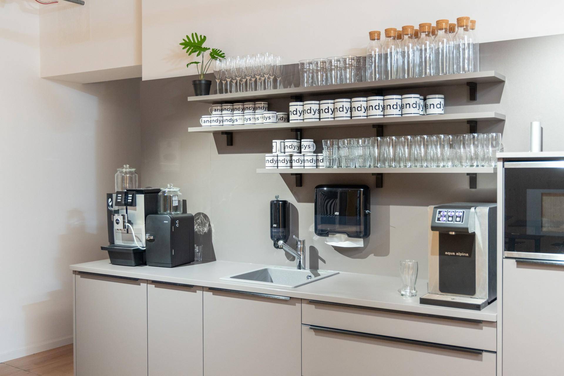 Moderne Teeküche mit Spüle, Kaffeemaschine und Wasserspender, ausgestattet mit Regalen und Gläsern.