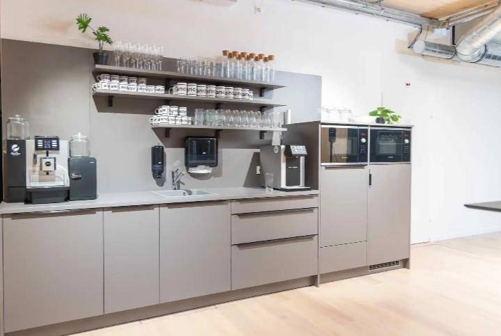 Funktionale Teeküche mit grauen Schränken, Mikrowelle und Kaffeemaschine, mit hellem Holzfußboden.