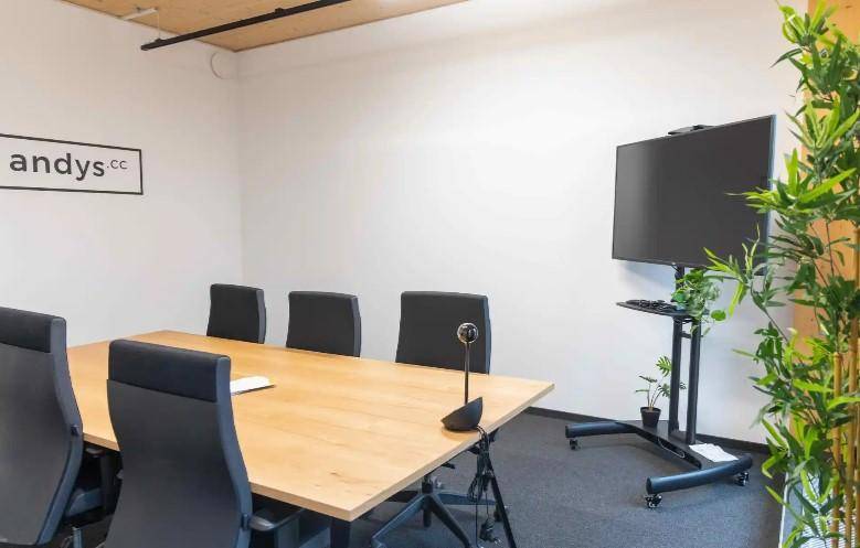 Moderner Besprechungsraum mit großem Tisch, Bürostühlen und einem Bildschirm, ideal für Präsentationen.