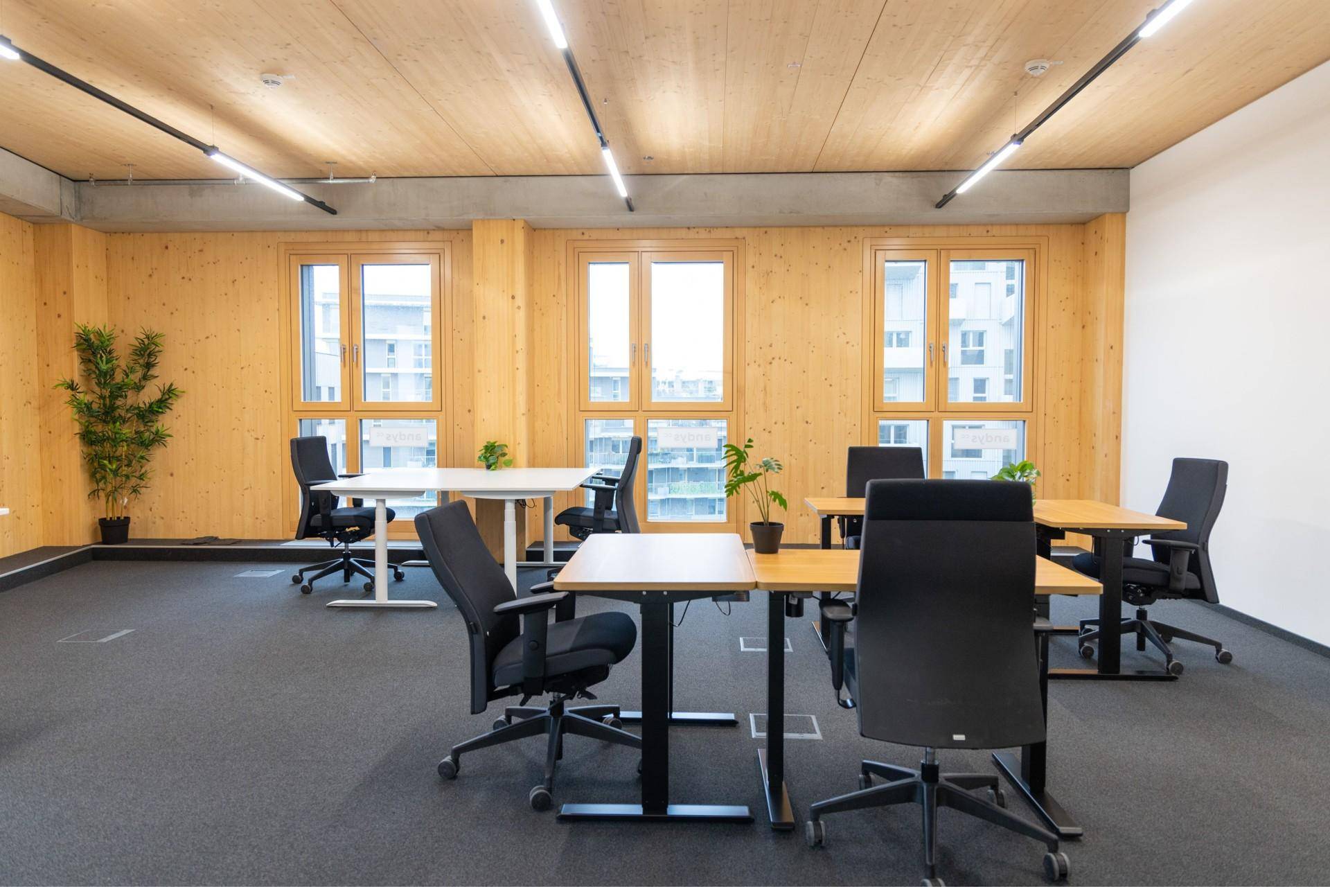 Geräumiges Büro mit mehreren modernen Arbeitsplätzen, Holzelementen und großen Fenstern für viel Tageslicht.