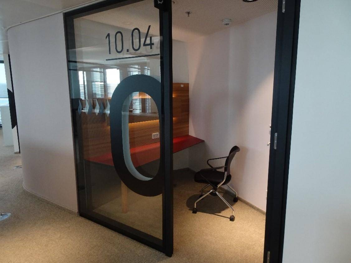Kleiner, privater Büroraum mit Glastür, Schreibtisch und Bürostuhl, ideal für konzentriertes Arbeiten.