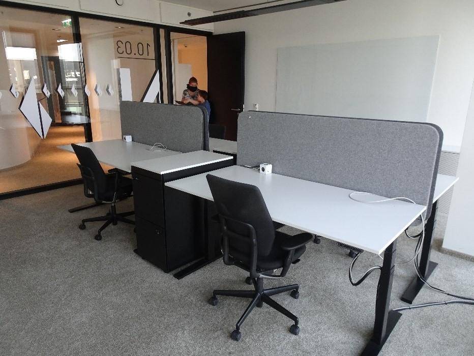 Offener Bürobereich mit modernen Schreibtischen, ergonomischen Stühlen und Teppichboden, gut beleuchtet.