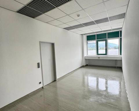 Leerer Büroraum mit großen Fenstern, die einen Blick auf die Berge und eine Dachfläche bieten.