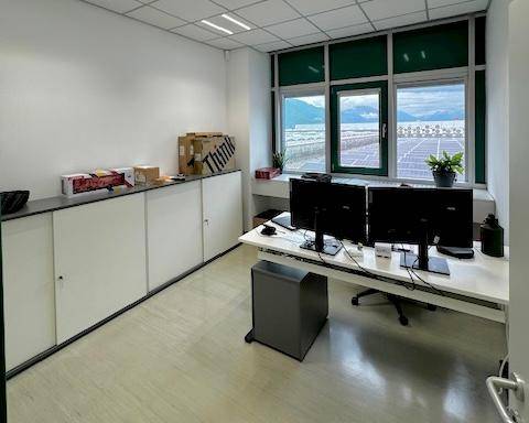 Büroraum mit Schreibtisch, Stauraum und großem Fenster mit Blick auf eine Solaranlage und Berge.