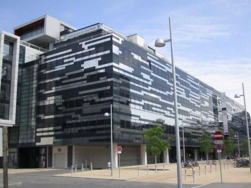 Detailansicht der modernen Glasfassade des Bürogebäudes mit reflektierenden Oberflächen und städtischer Umgebung.