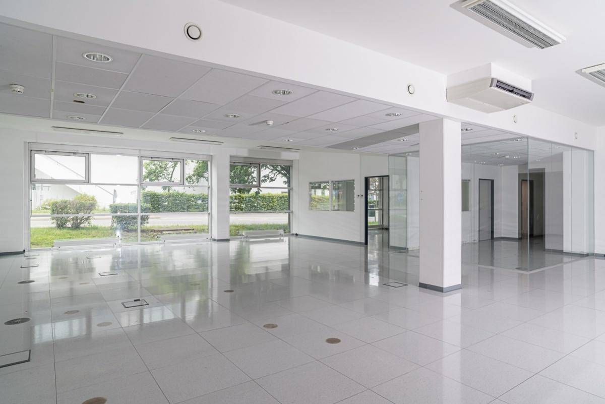Großer, leerer Büroraum mit hellen Fliesen, großen Fenstern und integrierter Klimaanlage.