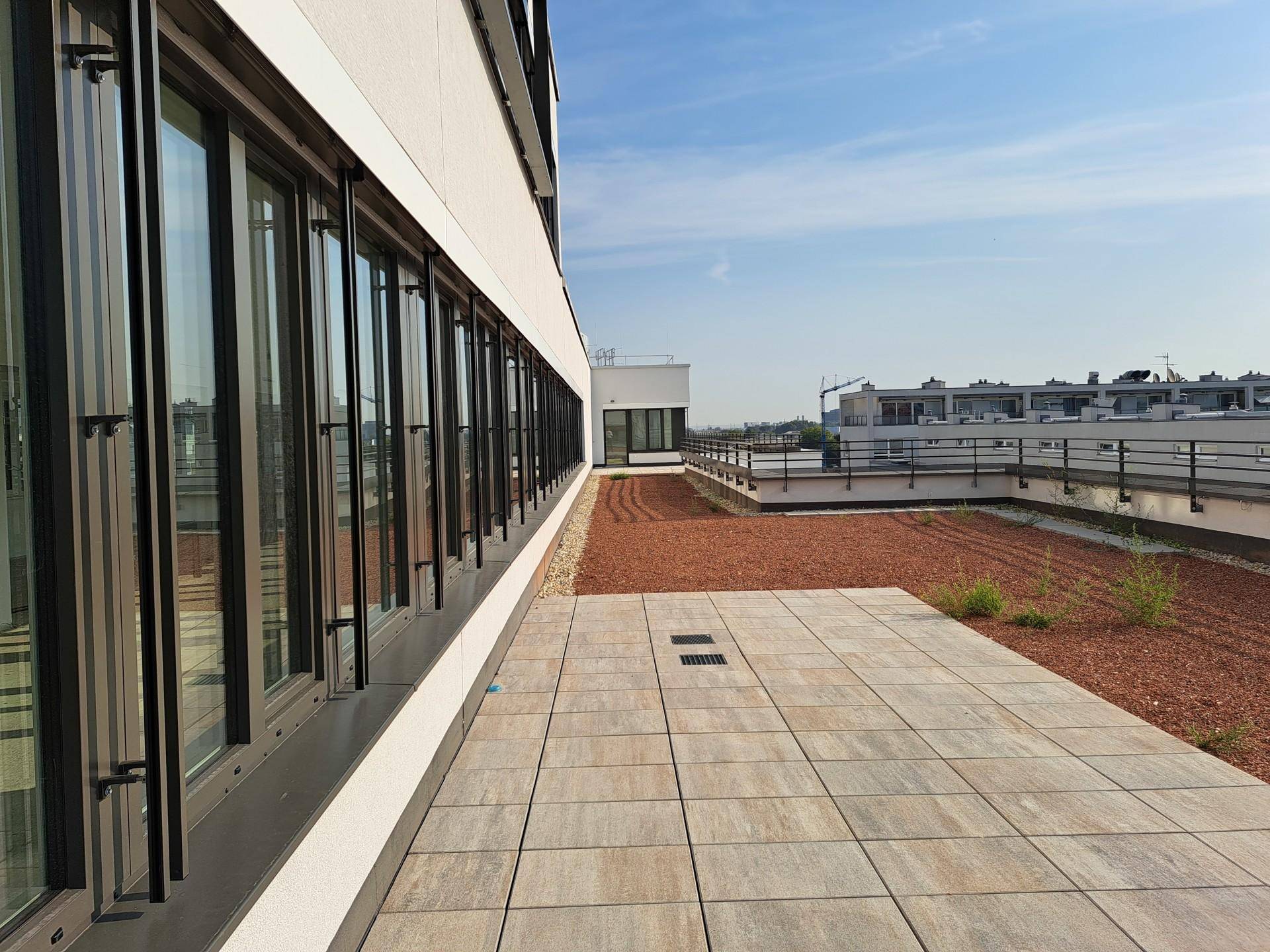 Moderne Dachterrasse mit großen Fenstern, gefliestem Bereich und Blick über die Stadt.