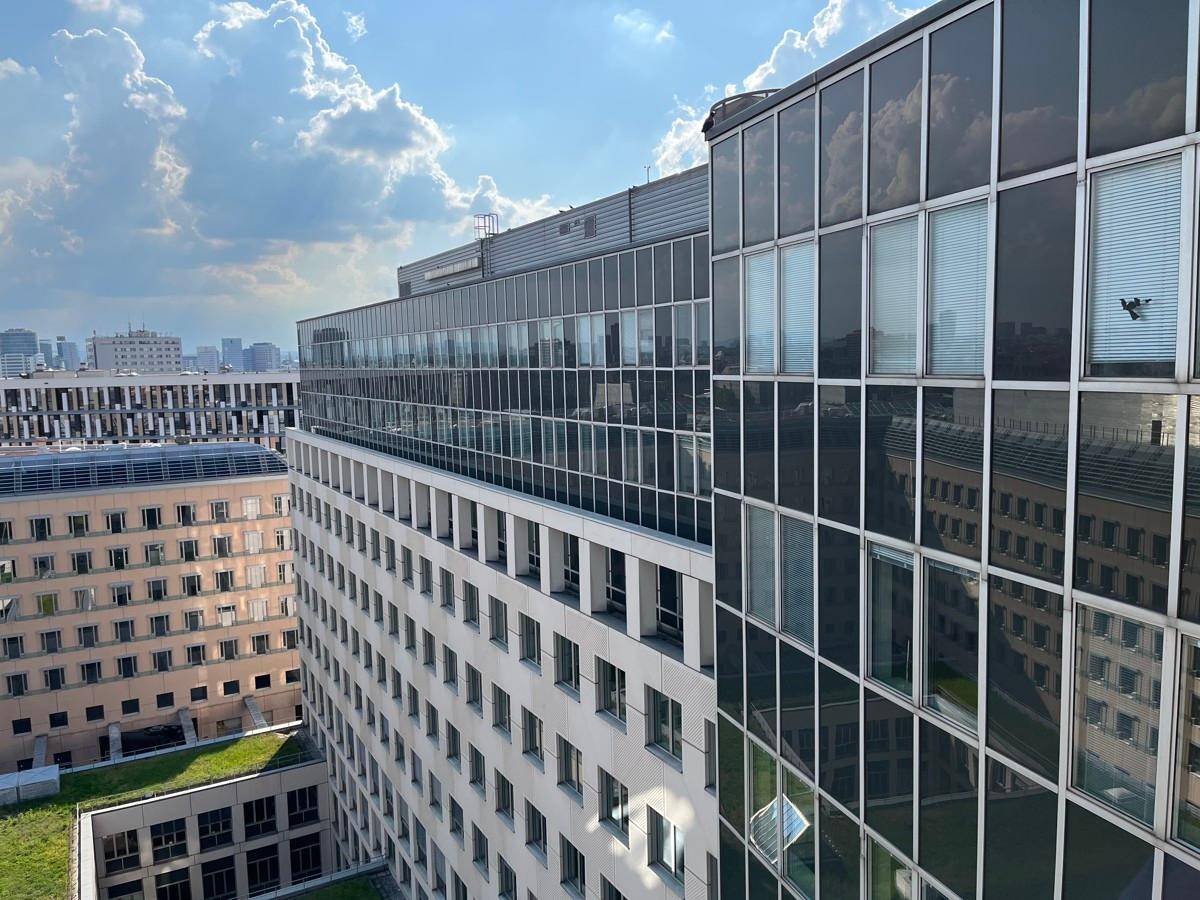 Moderne Glasfassade eines Bürogebäudes mit reflektierenden Fenstern unter blauem Himmel.