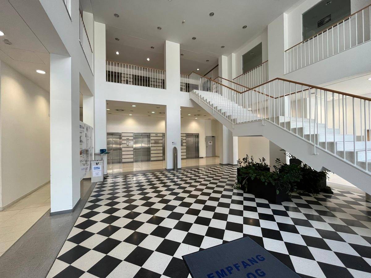 Geräumige Lobby mit markantem Schachbrettmuster-Boden, breiter Treppe und mehreren Aufzügen.