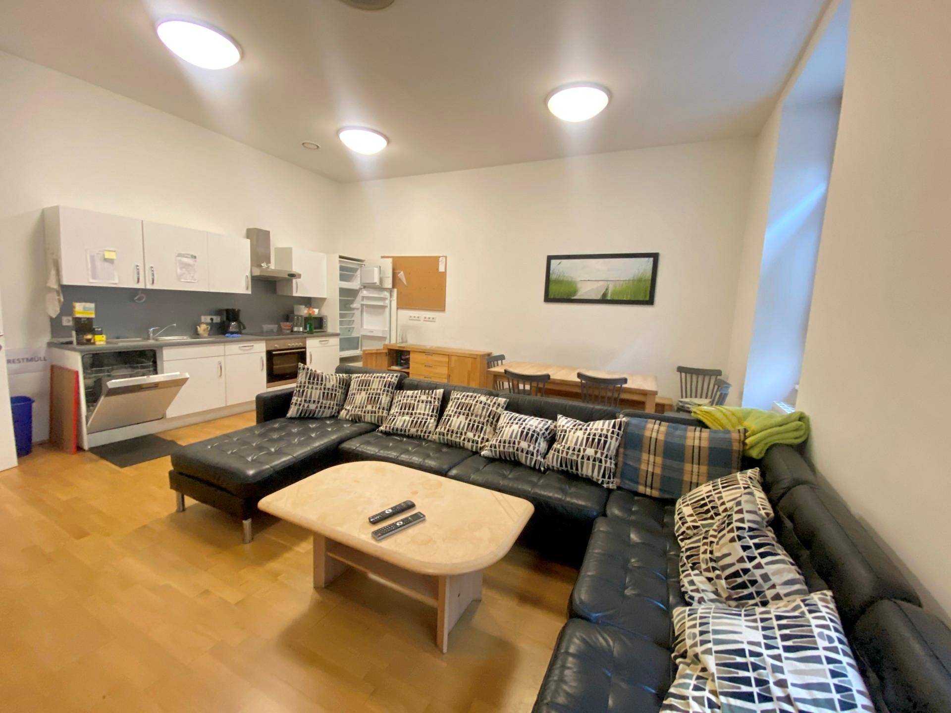 Gemeinschaftsraum mit integrierter Küche, großem Sofa und Holzboden, ideal für Pausen.