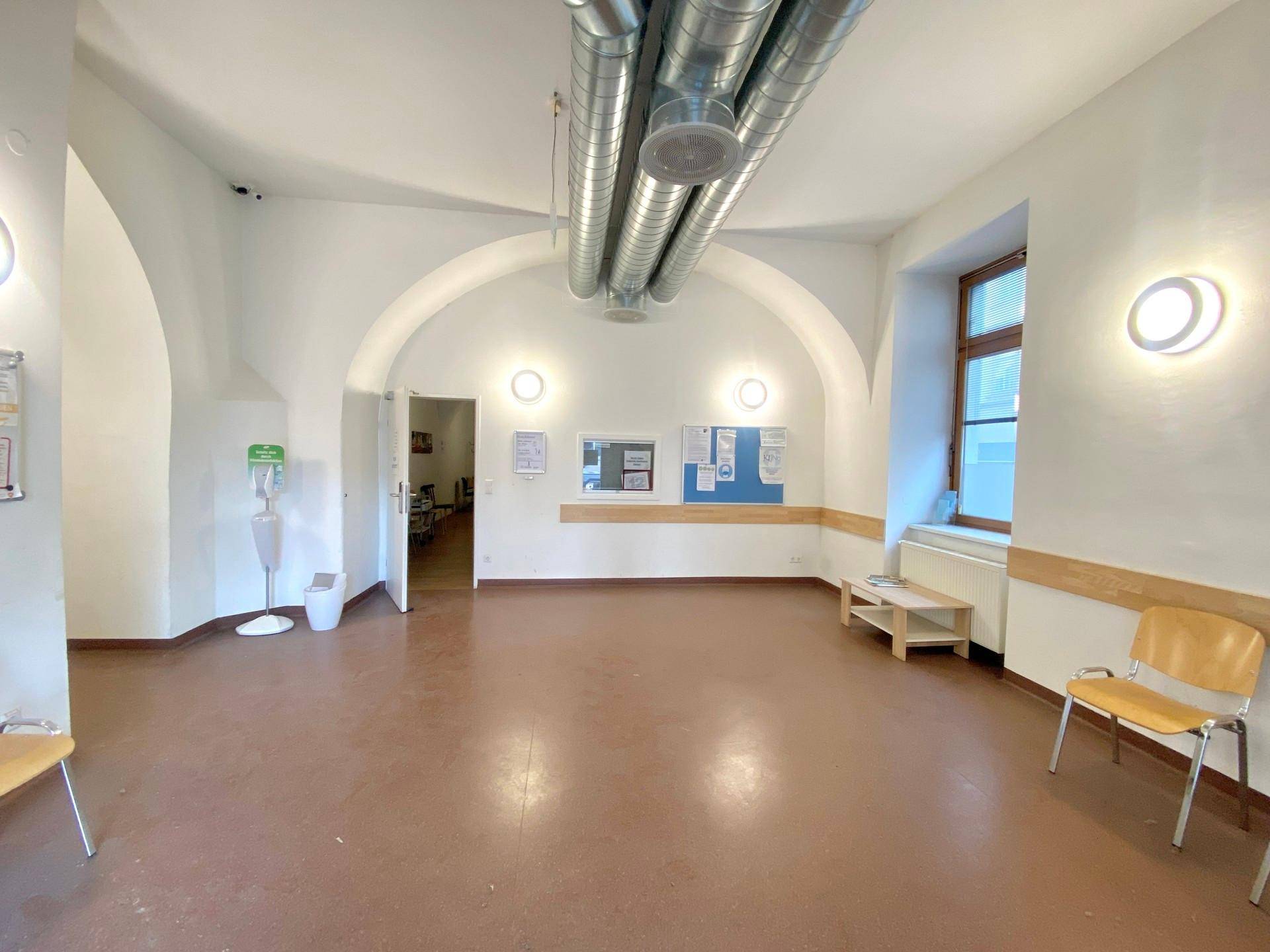 Geräumiger Wartebereich mit gewölbter Decke, sichtbaren Lüftungsrohren und Linoleumboden.