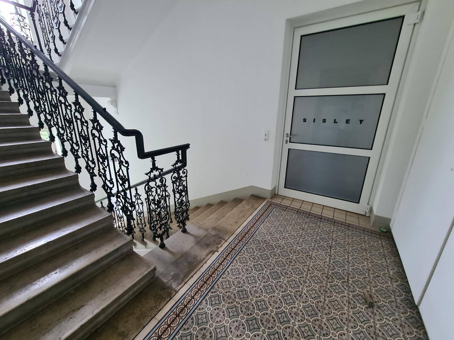 Historisches Treppenhaus mit kunstvollem schmiedeeisernem Geländer und gemusterten Fliesen im Eingangsbereich.
