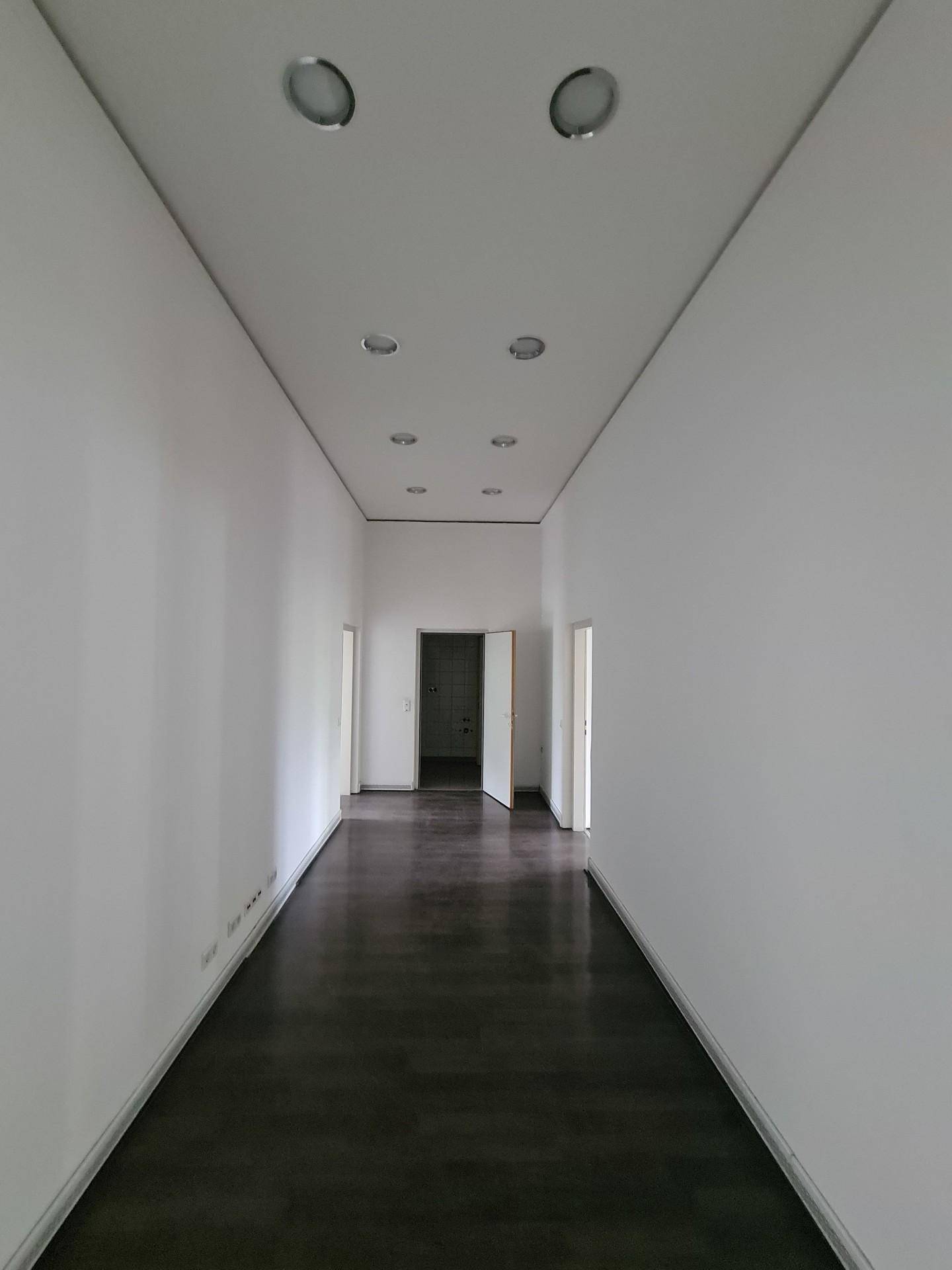 Moderner Flur mit dunklem Boden und Einbaustrahlern in der Decke, der zu weiteren Räumen führt.