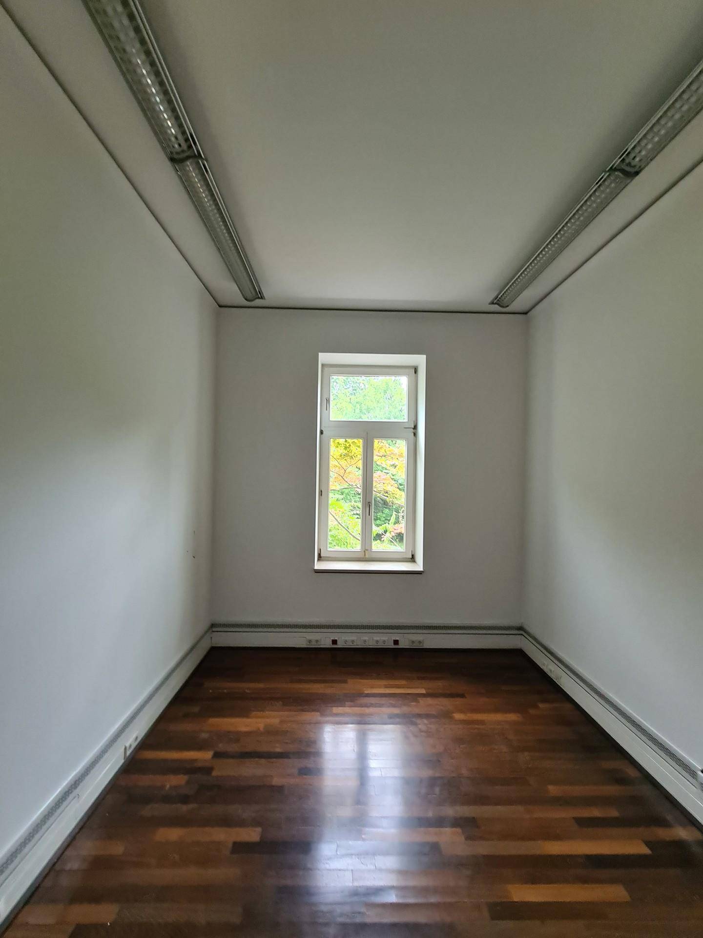 Kleiner, heller Büroraum mit Holzboden und einem Fenster mit Blick ins Grüne.