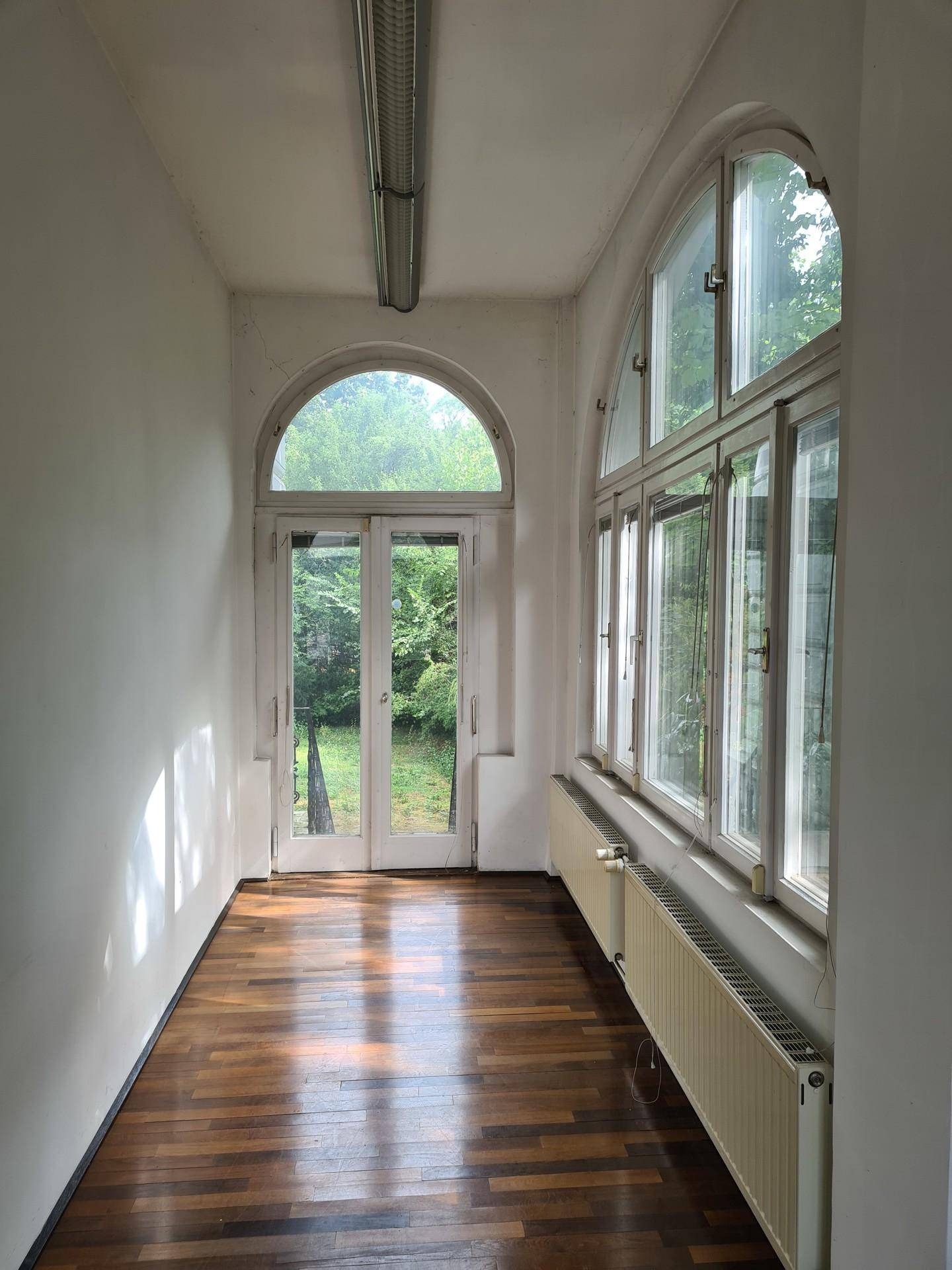 Langer Flur mit Holzboden, hohen Rundbogenfenstern und Blick in den Garten.