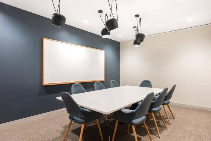 Moderner Konferenzraum mit langem weißen Tisch, blauen Stühlen und einer dunklen Akzentwand.