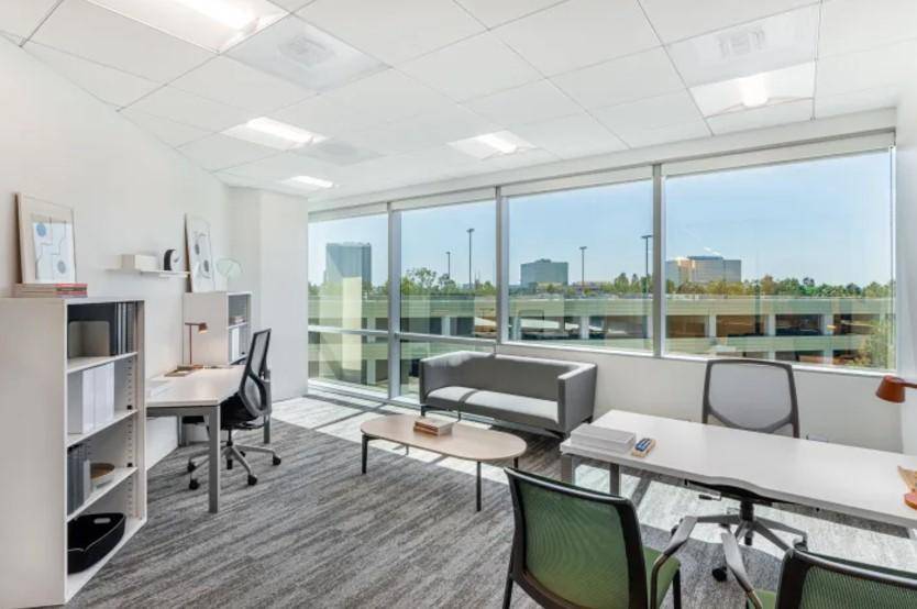 Helles Büro mit großen Fenstern, Teppichboden und Blick auf die umliegende Bebauung.