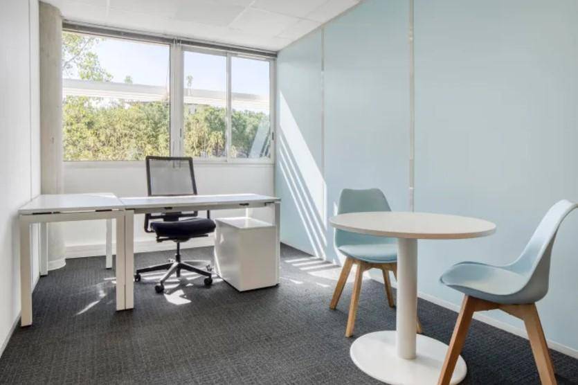 Privates Büro mit Schreibtisch, Besprechungstisch und großen Fenstern mit Blick ins Grüne.