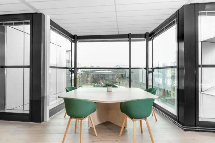 Heller Besprechungsraum mit großen Fenstern, modernem Tisch und grünen Stühlen, bietet Weitblick.