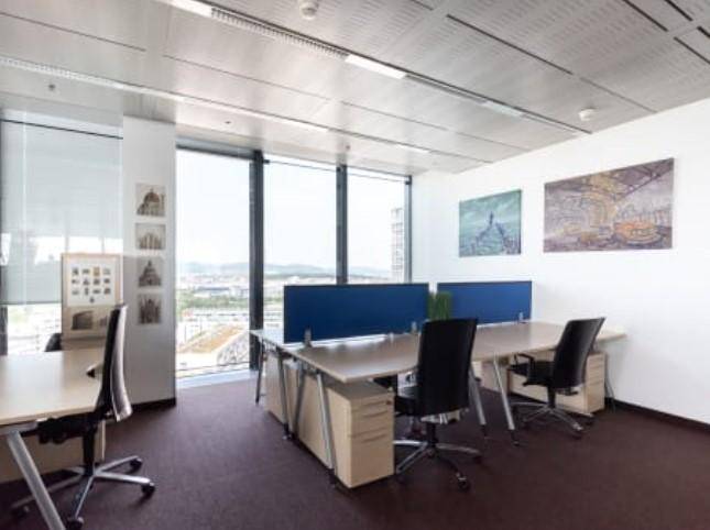 Offener Bürobereich mit mehreren Arbeitsplätzen, großen Fenstern und Panoramablick über die Stadt.