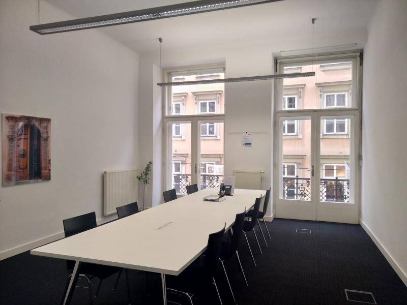 Großer Konferenzraum mit einem langen Tisch und vielen Stühlen, hell durch hohe Fenster mit Blick auf die Stadt.