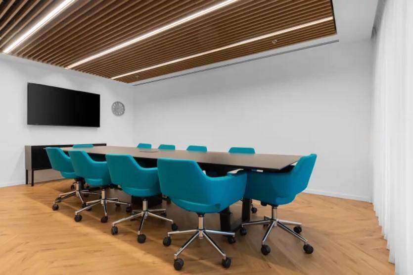 Heller Konferenzraum mit modernem Holzlattendecke, großem Bildschirm und ergonomischen Stühlen.