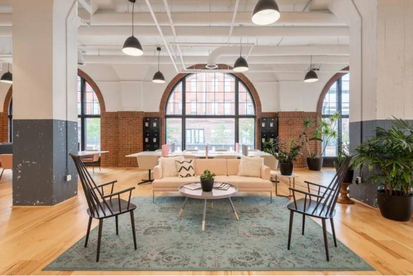 Geräumiger Lounge-Bereich in einem Loft-Büro mit hohen Decken, großen Bogenfenstern und Holzboden.