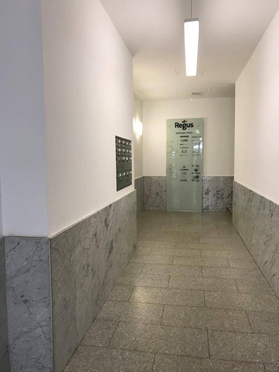 Heller Flur mit Marmorverkleidung und Terrazzoboden, der zu einem Büro führt.