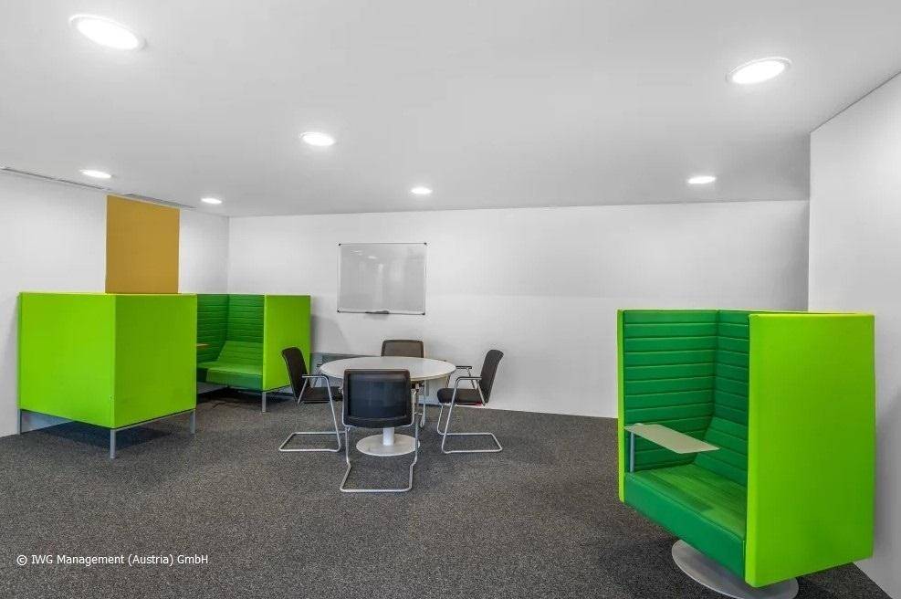 Kreativer Arbeitsbereich mit grünen Sitzkabinen, einem runden Tisch und Whiteboard für Kollaboration.