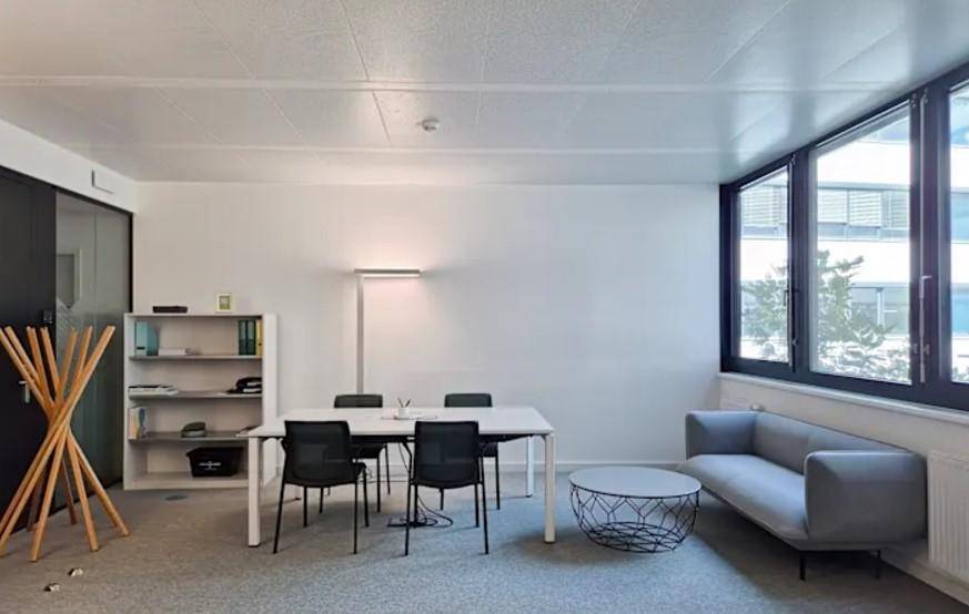 Geräumiges Büro mit Teppichboden, großen Fenstern und moderner Einrichtung für Besprechungen.