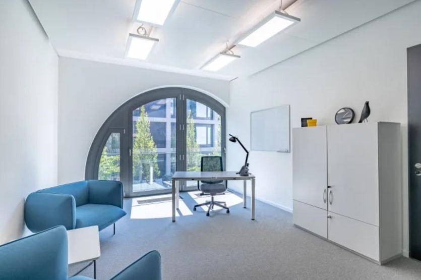 Modernes Büro mit einzigartigem Bogenfenster, Schreibtisch und bequemen blauen Sesseln mit Blick ins Grüne.