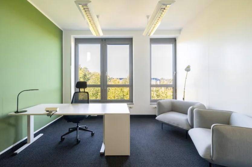 Helles Einzelbüro mit grüner Akzentwand, Schreibtisch und bequemen grauen Sesseln mit Blick ins Grüne.