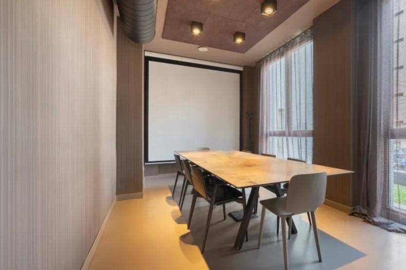 Moderner Konferenzraum mit großem Tisch, Projektionsleinwand und industriellen Deckenelementen.
