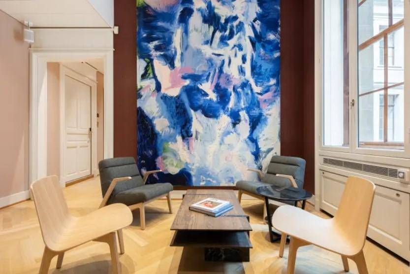 Gemütlicher Loungebereich mit modernen Sesseln, Holzboden und großem Kunstwerk an der Wand.