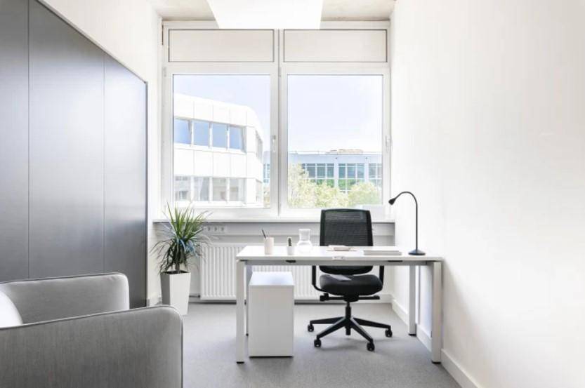 Helles Einzelbüro mit großem Fenster, Schreibtisch und Bürostuhl.